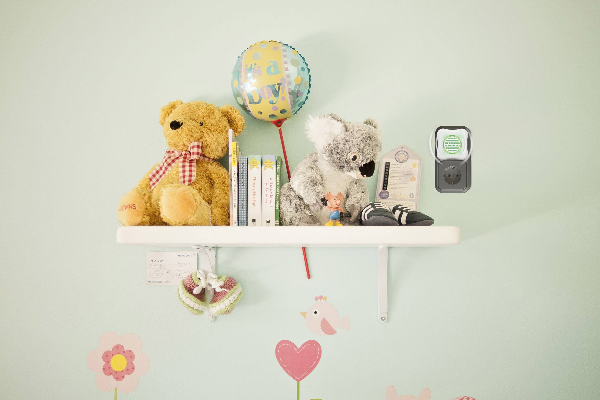 A shelf in the children's bedroom with two soft toys, books and a 'baby' balloon. Below it, wall stickers of flowers and birds.