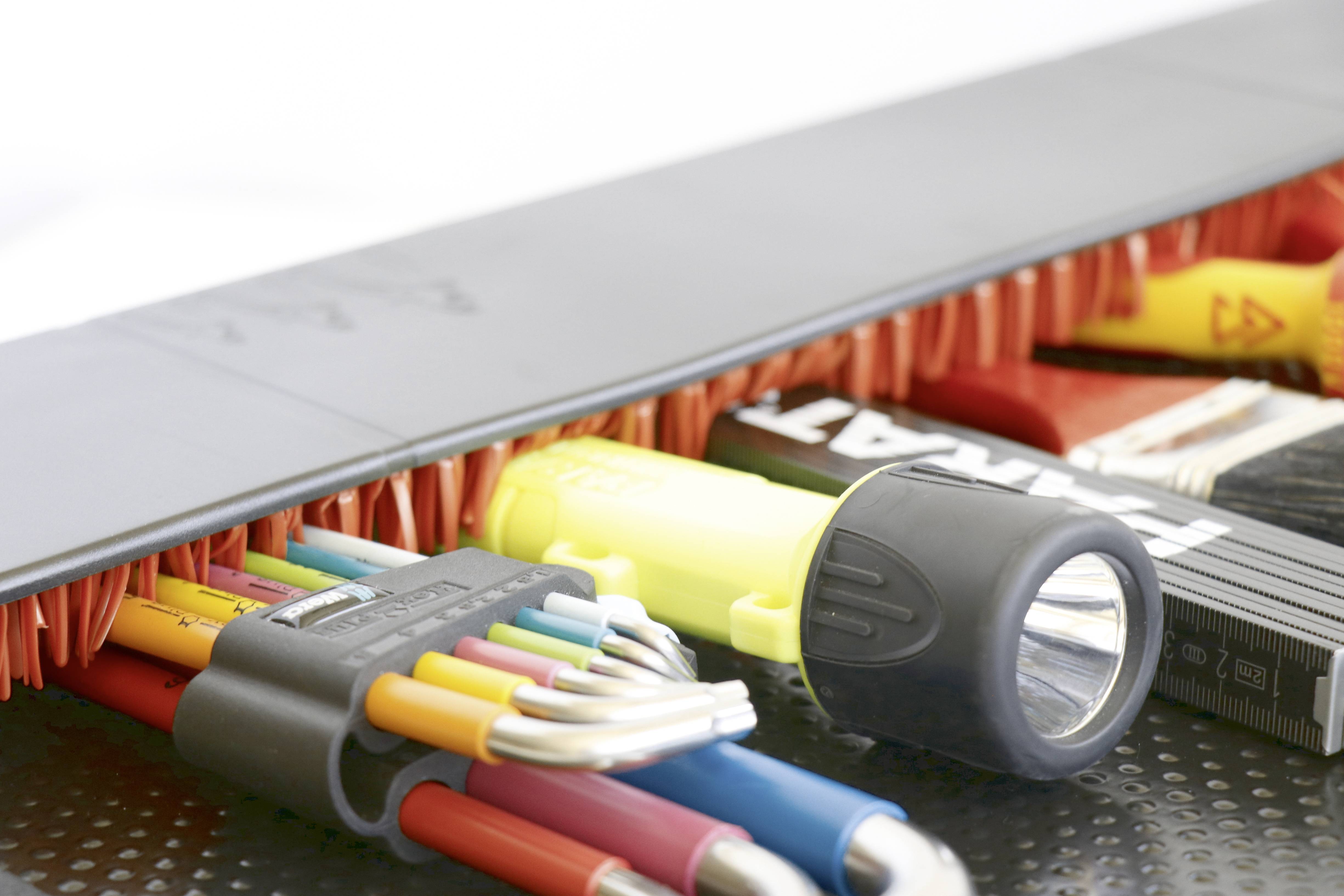 "A close-up of various tools, including colourful cables, a torch, and a brush, lying neatly side by side."<br><br>Note the British English spelling of:<br>- "colourful" instead of "colorful"<br>- "torch" instead of "flashlight"