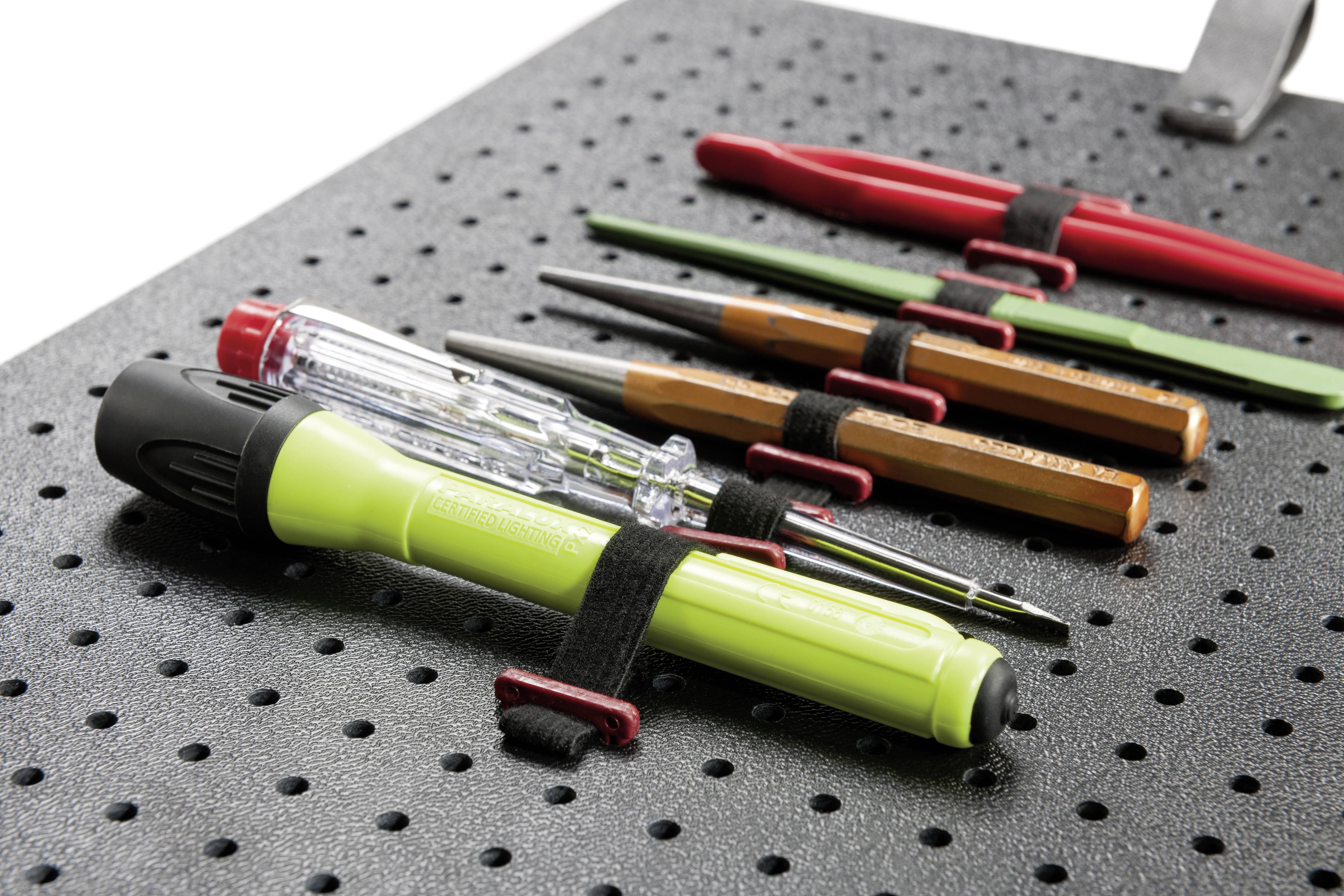 Several tools, including screwdrivers and pencils, are securely fastened with straps on a perforated board.