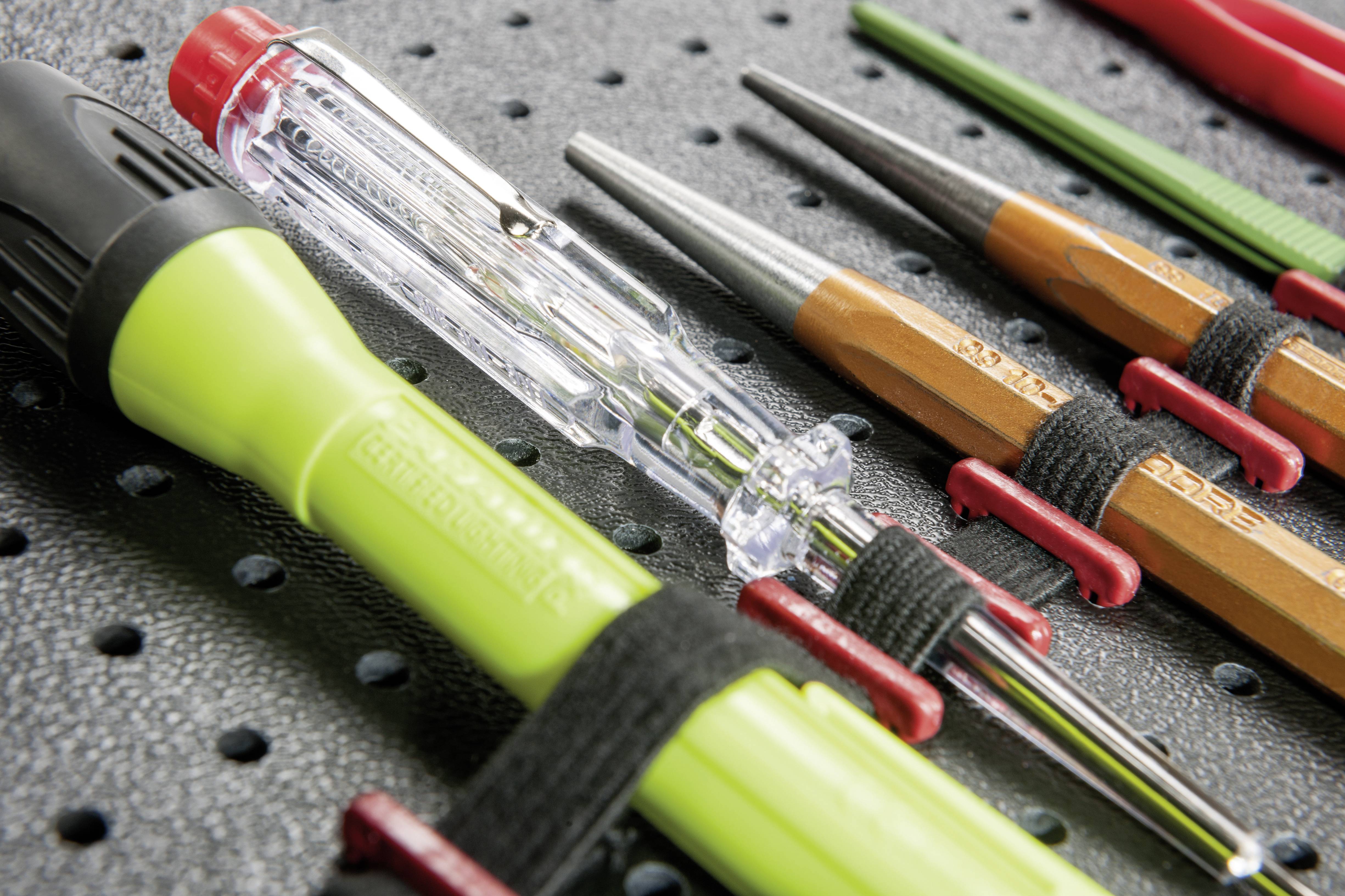 Various tools, including a green screwdriver and a voltage tester, are fastened to a black tool board.