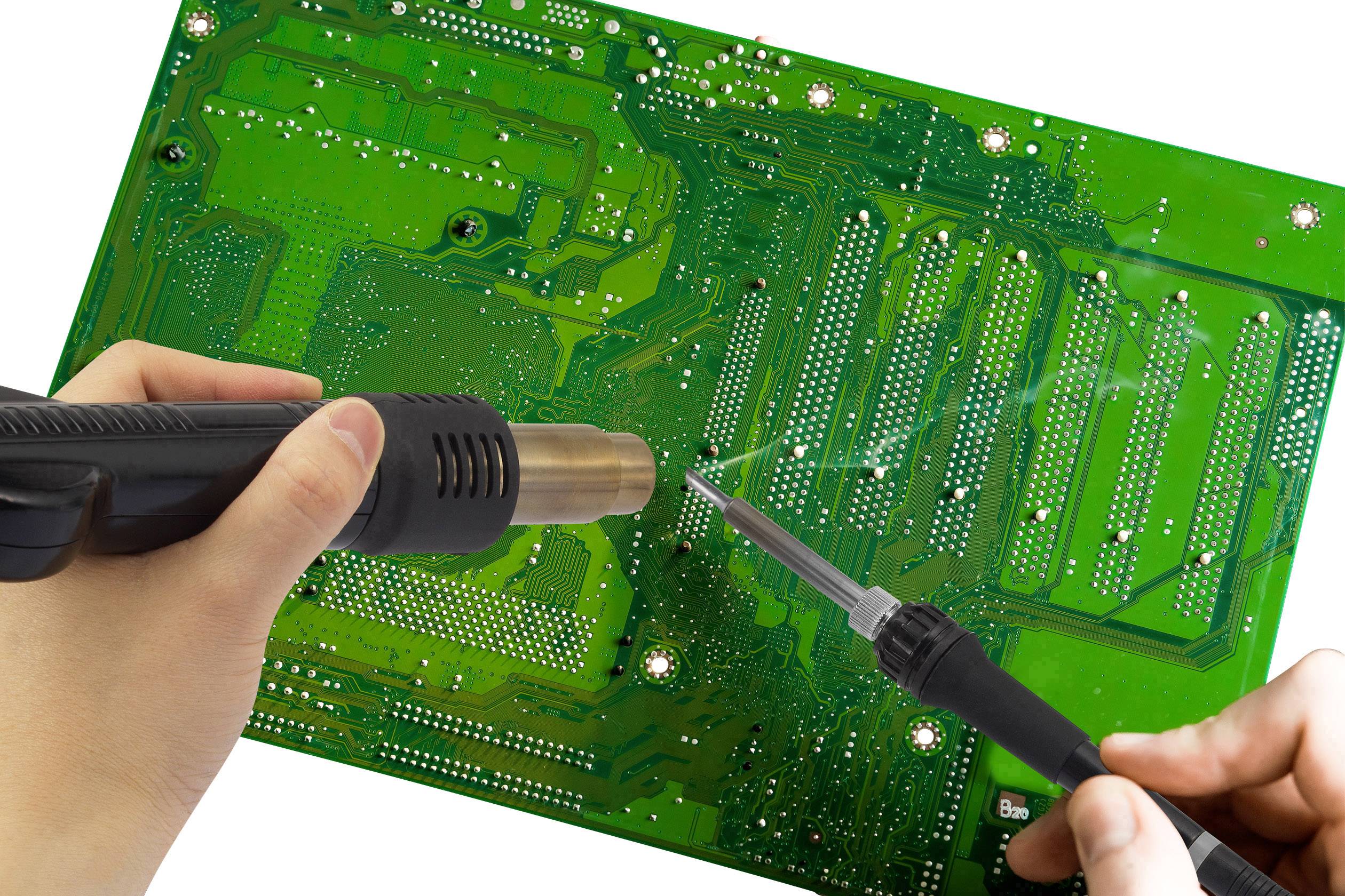 A person is soldering with a soldering iron and a hot air gun on a green circuit board.