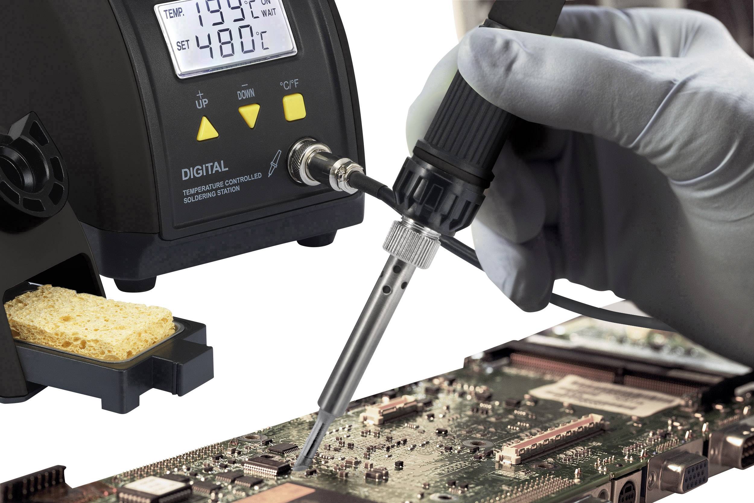 A person is soldering with a soldering iron on a circuit board. The display of the soldering station shows the current temperature and set point.