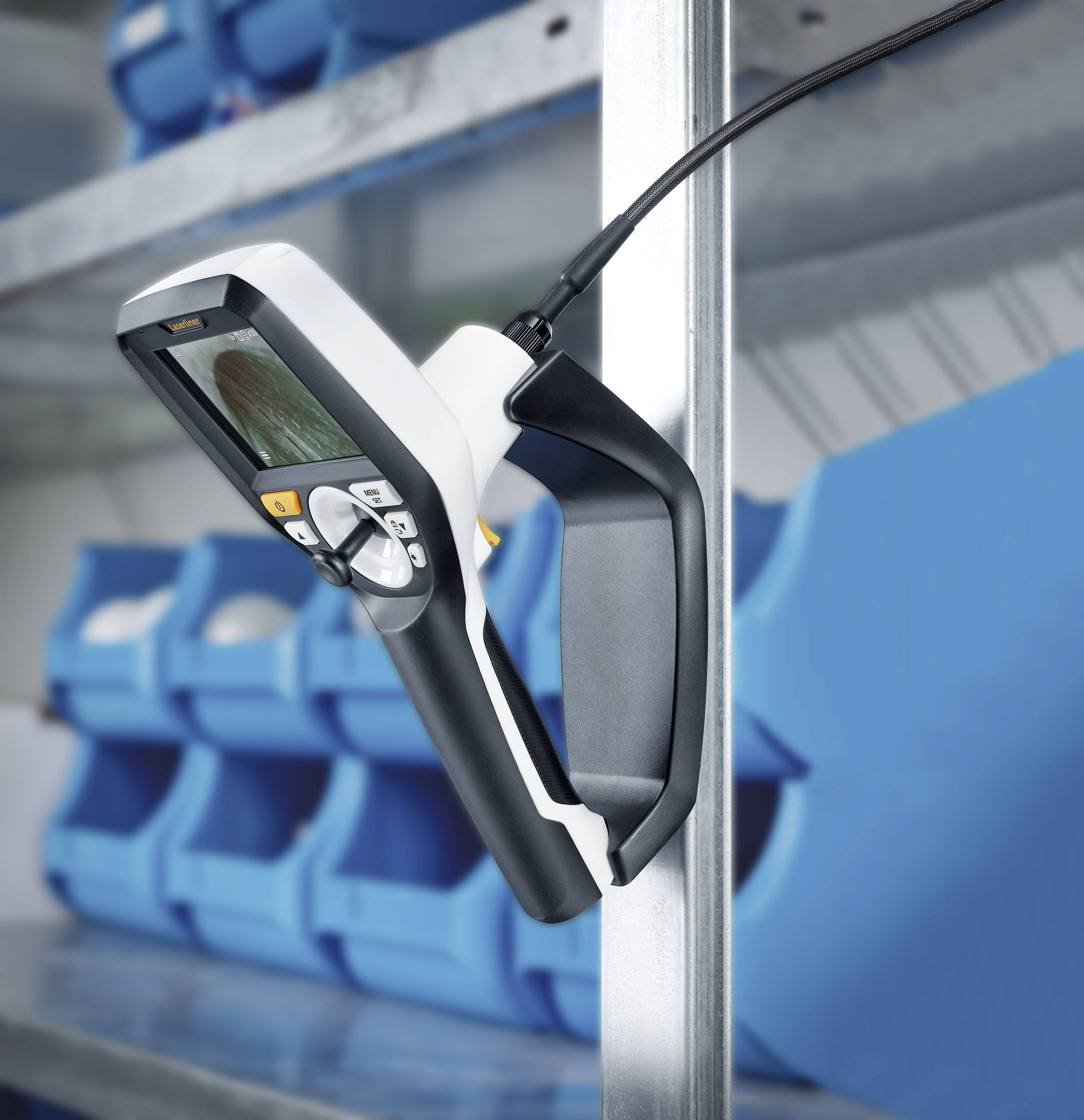 Handheld device with display, mounted on a shelf, surrounded by blue plastic containers. Likely used for measurement or inspection.