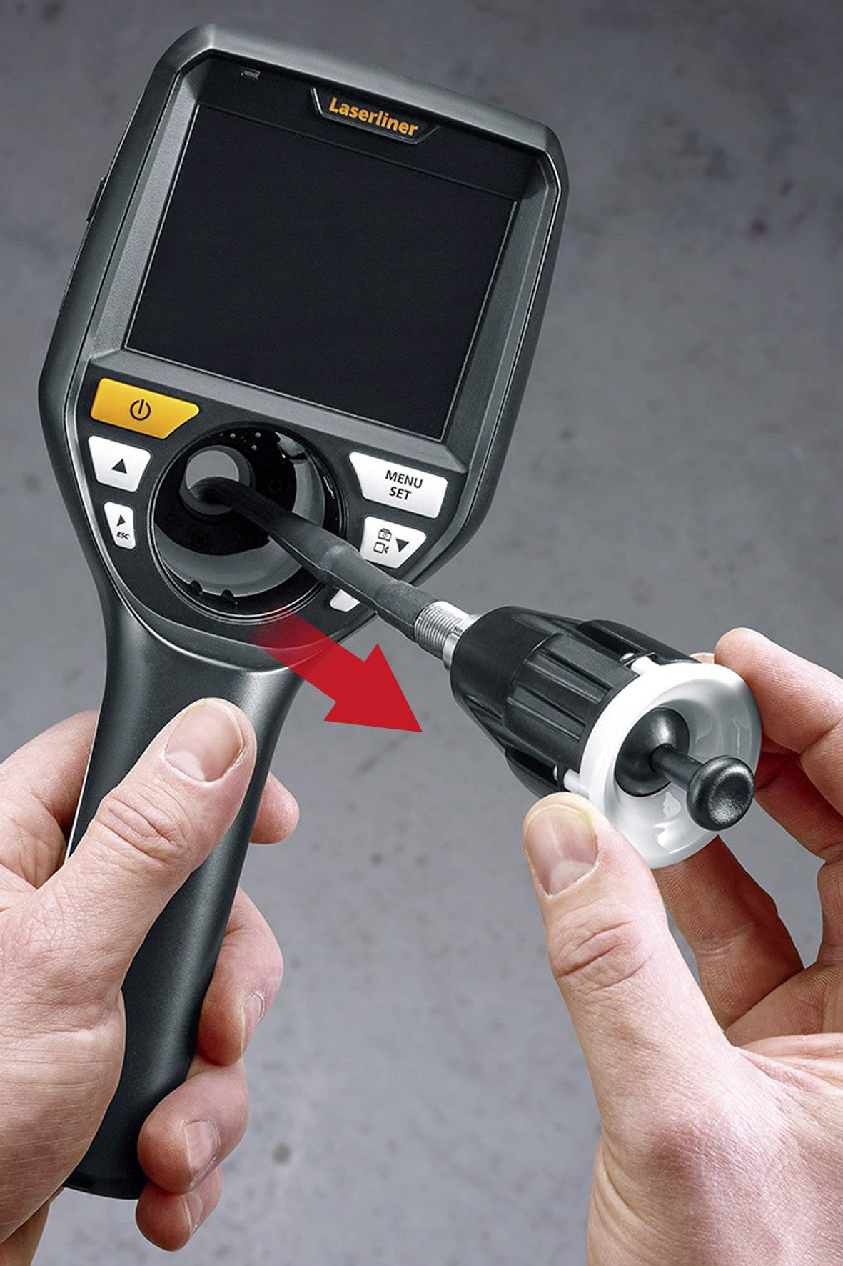 A hand is holding an inspection device with a screen, while the other hand is inserting a cable with a camera into the socket on the device.