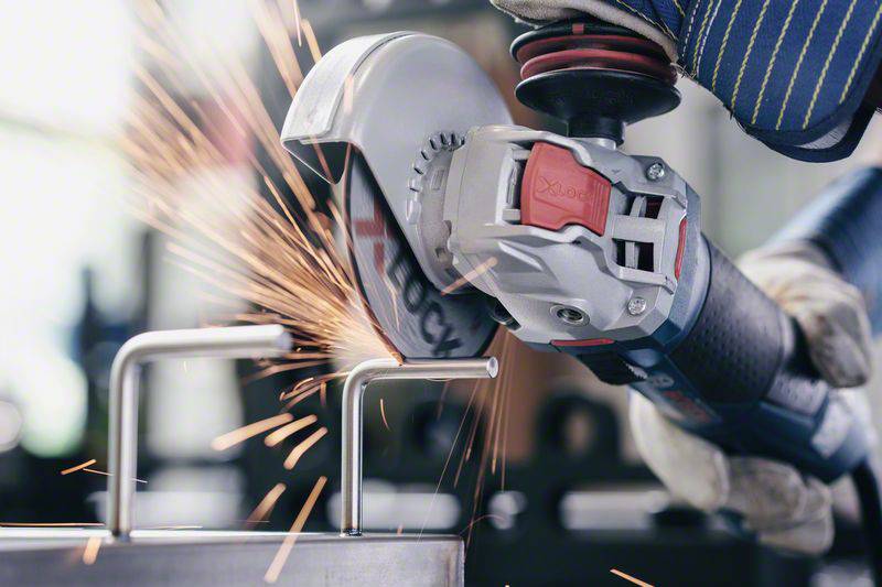 A hand holds an angle grinder, generating sparks while working on a metal piece. Wearing protective gloves.