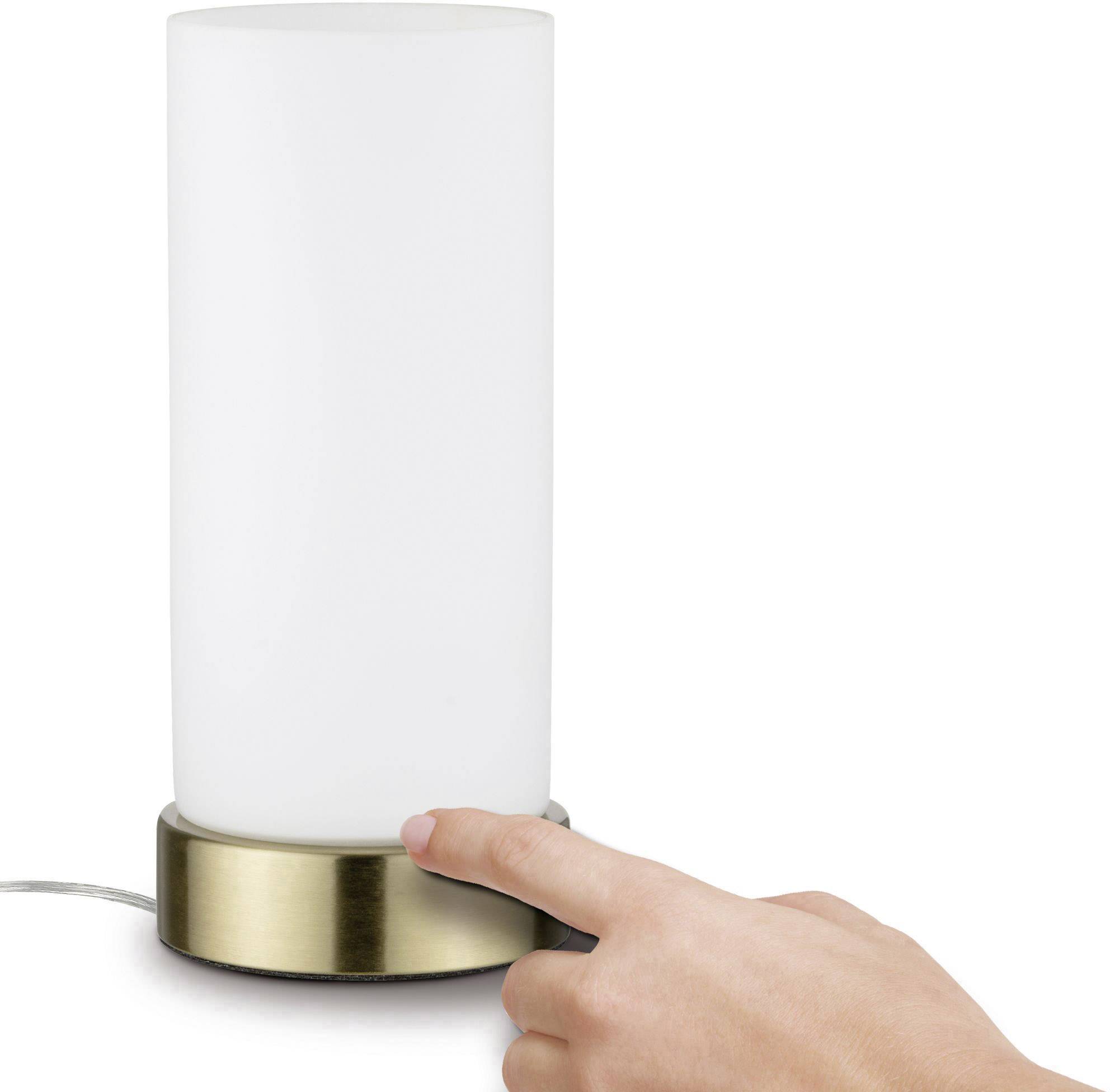 A hand touches the base of a cylindrical lamp with frosted glass and a metallic stand on a table.