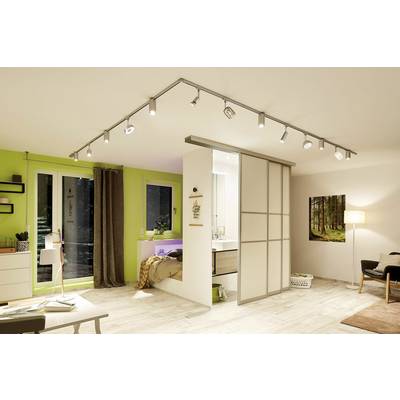A modern living room with a sliding door to the bedroom, light wooden flooring, green wall, desk, and ceiling spotlights.