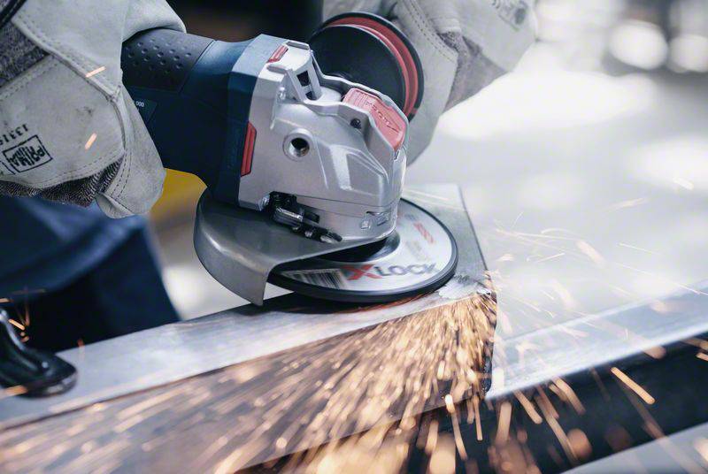 A person is grinding a piece of metal with an angle grinder. Sparks are flying in a workshop environment.