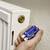 A hand holds a radiator key in front of a white radiator. The key is placed on the valve to release air.