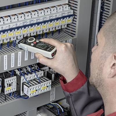 A person is checking the wiring in an electrical cabinet using a digital measuring device. The electrical cabinet contains multiple fuses and cables.