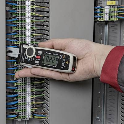 A hand is holding a multimeter connected to an open electrical cabinet to measure the electrical voltage.