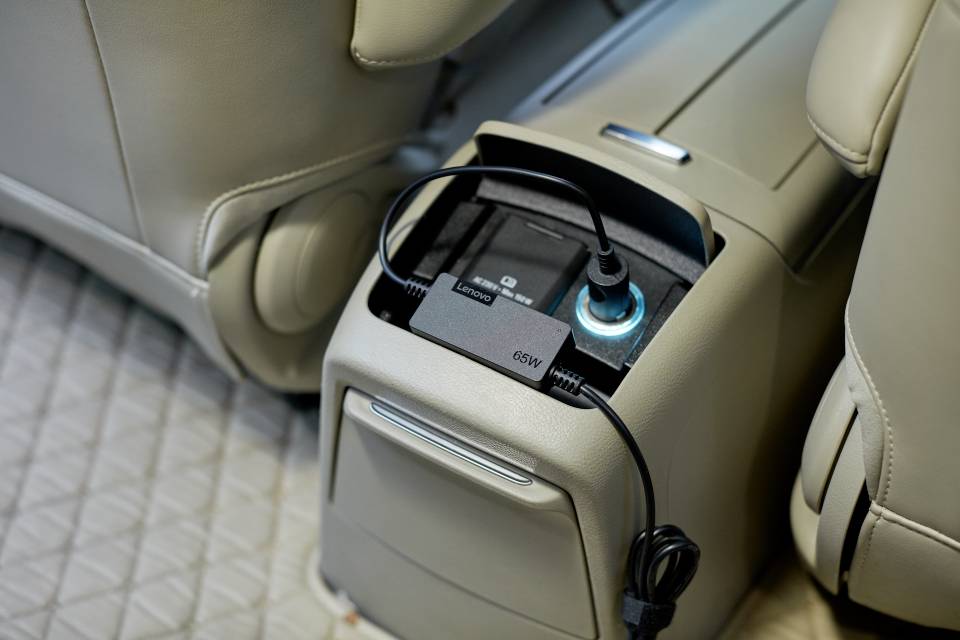 A black cable is plugged into a socket in the rear seating area of a car, positioned above a closed storage compartment.