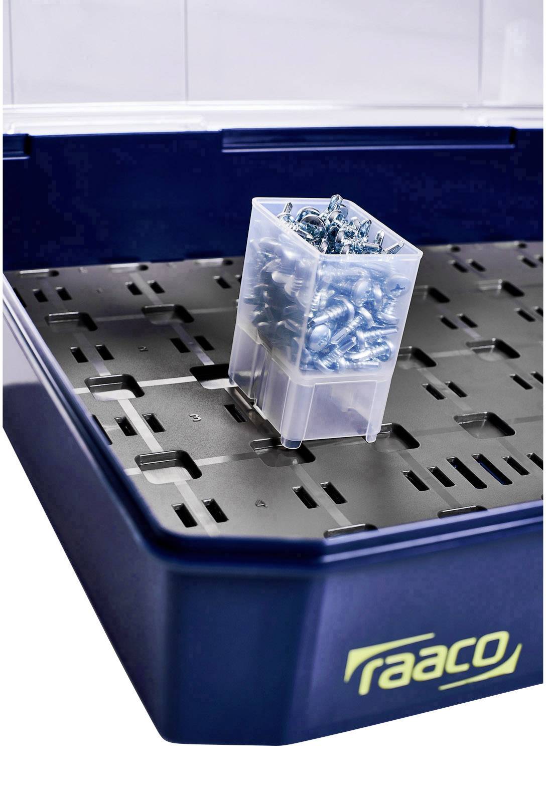 A dark blue storage box by 'raaco' with a transparent container full of metal parts on the black interior surface.