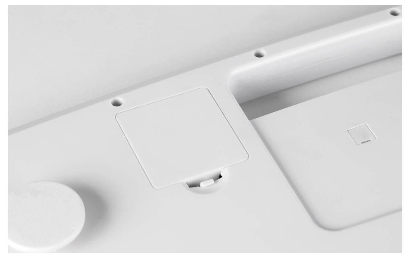 White underside of an electronic device with battery cover and screw recesses.