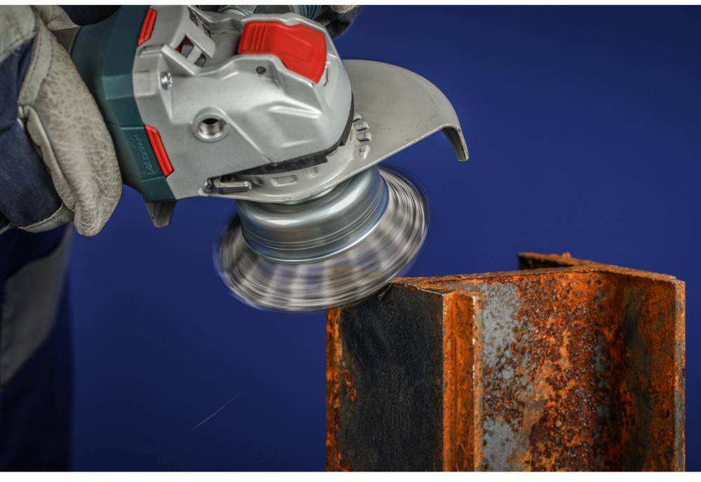 A person is using an angle grinder to remove rust from a metal block. The metal block is partially heavily rusted.