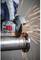 A worker cuts through a metal pipe with an angle grinder. Sparks fly from the cutting area in different directions.