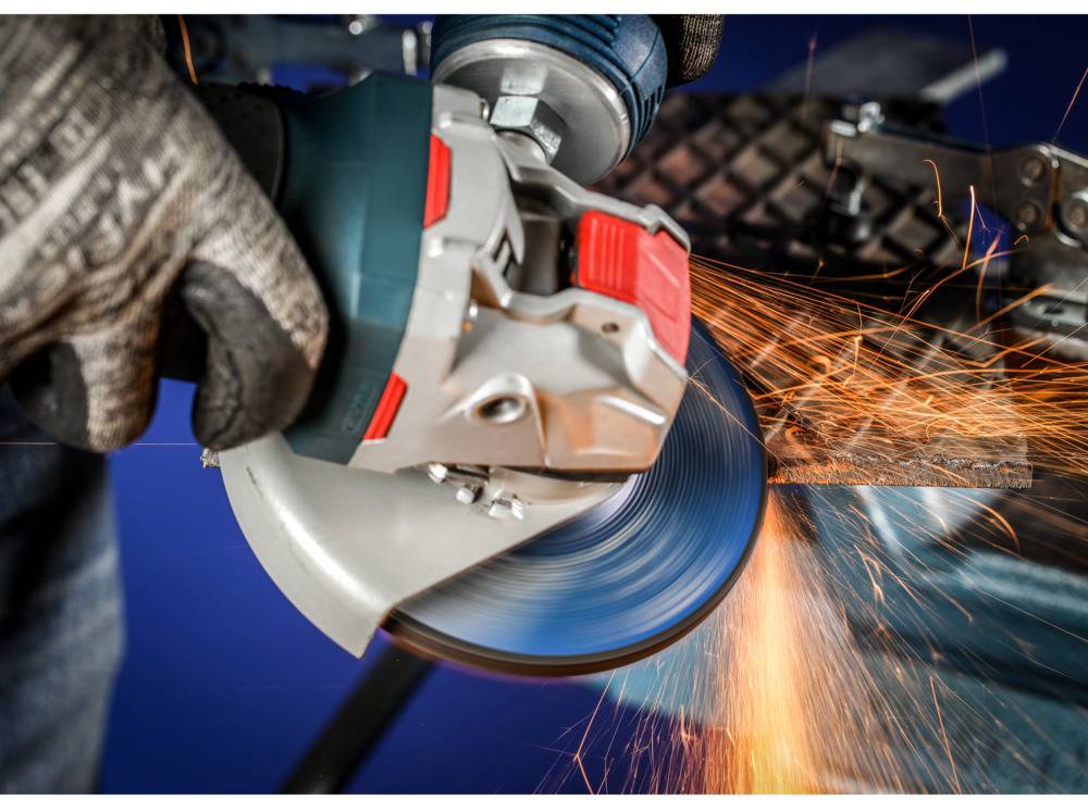 A person is grinding metal with an angle grinder. Sparks are flying from the point of contact. They are wearing protective gloves.