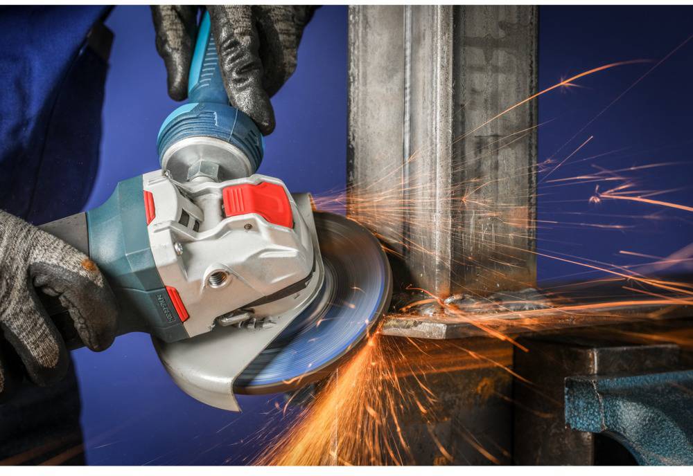 A person wearing work gloves is grinding a metal surface with an angle grinder, sparks flying, against a blue background.