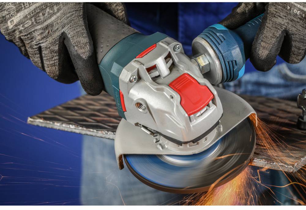A person is grinding a metal plate with an angle grinder, sparks flying. The device has a blue handle and red operating element, and they are wearing protective gloves.