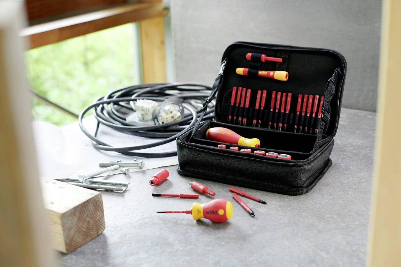 An open tool case with various screwdrivers on a table. Cables and metal fastening elements are lying beside it.