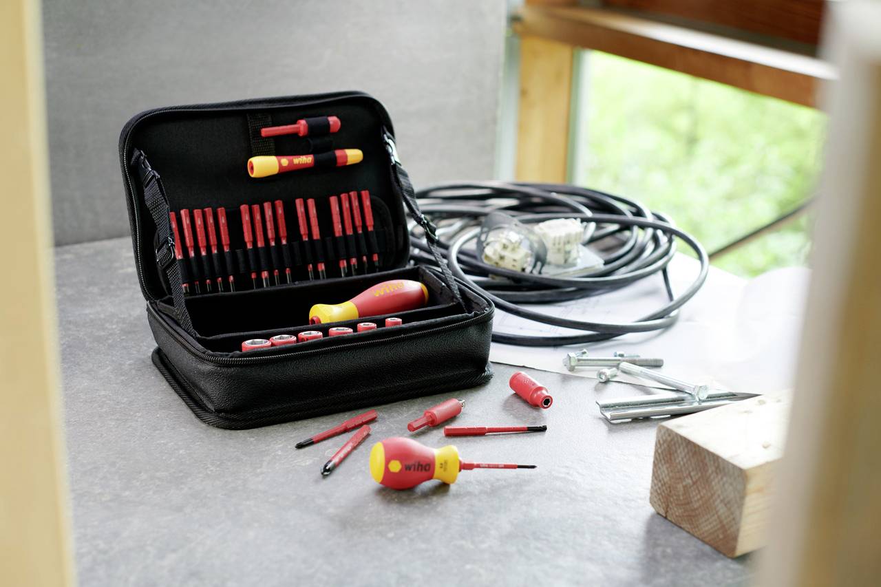 Screwdriver set with various bits next to a cable fuse and wooden beam. Work prospects on a light table in daylight.