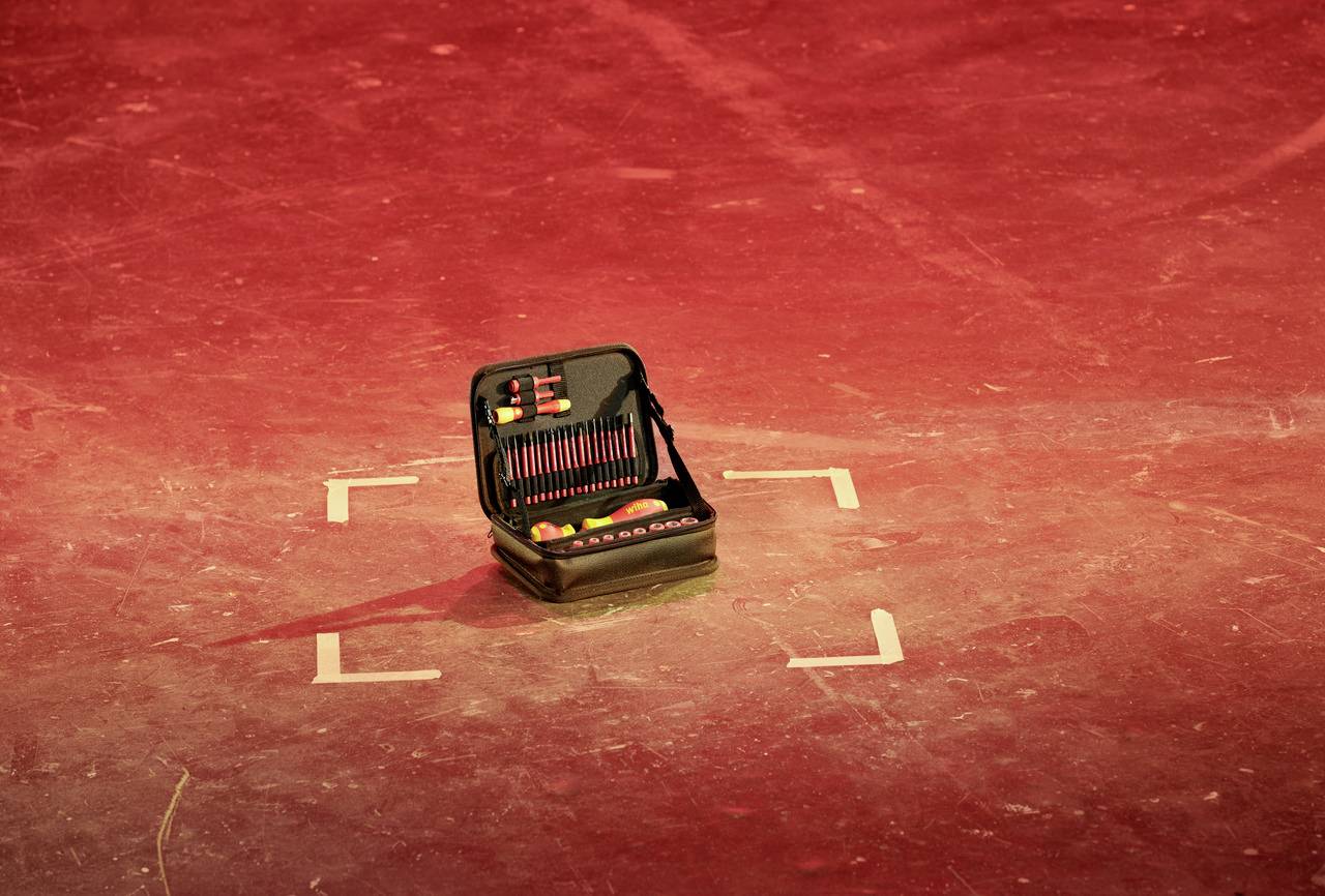 An open toolbox sits on a red-illuminated floor, surrounded by markings. Contains various tools.