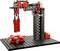 A robotic arm made of building blocks lifts a red block. It stands on a black perforated plate. The arm appears to be programmable.