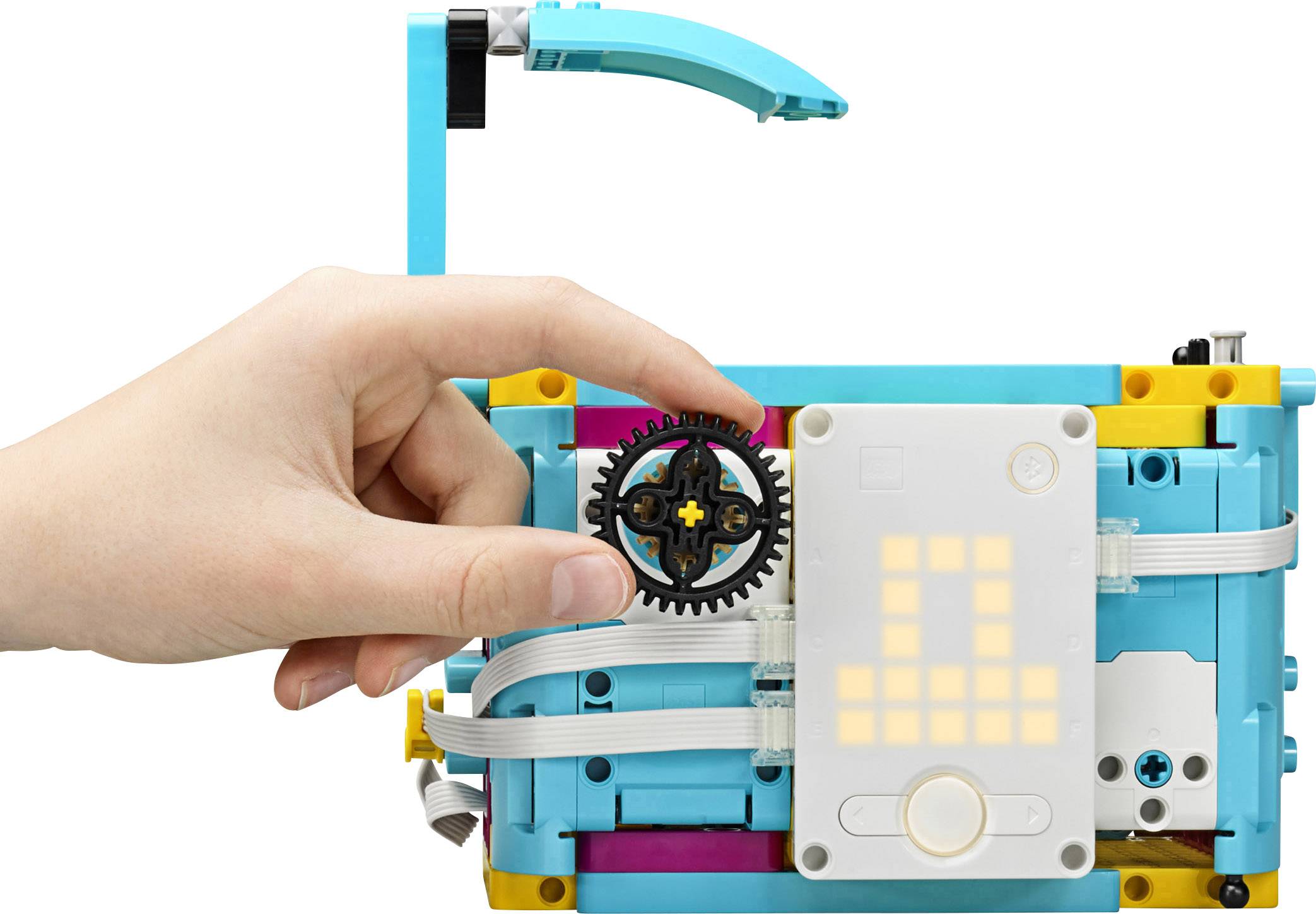 A hand turns a gear on an assembled robotics kit with a glowing display and cables.