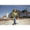 A worker wearing a hard hat and hi-vis vest stands on a construction site, with unfinished buildings and cranes in the background.
