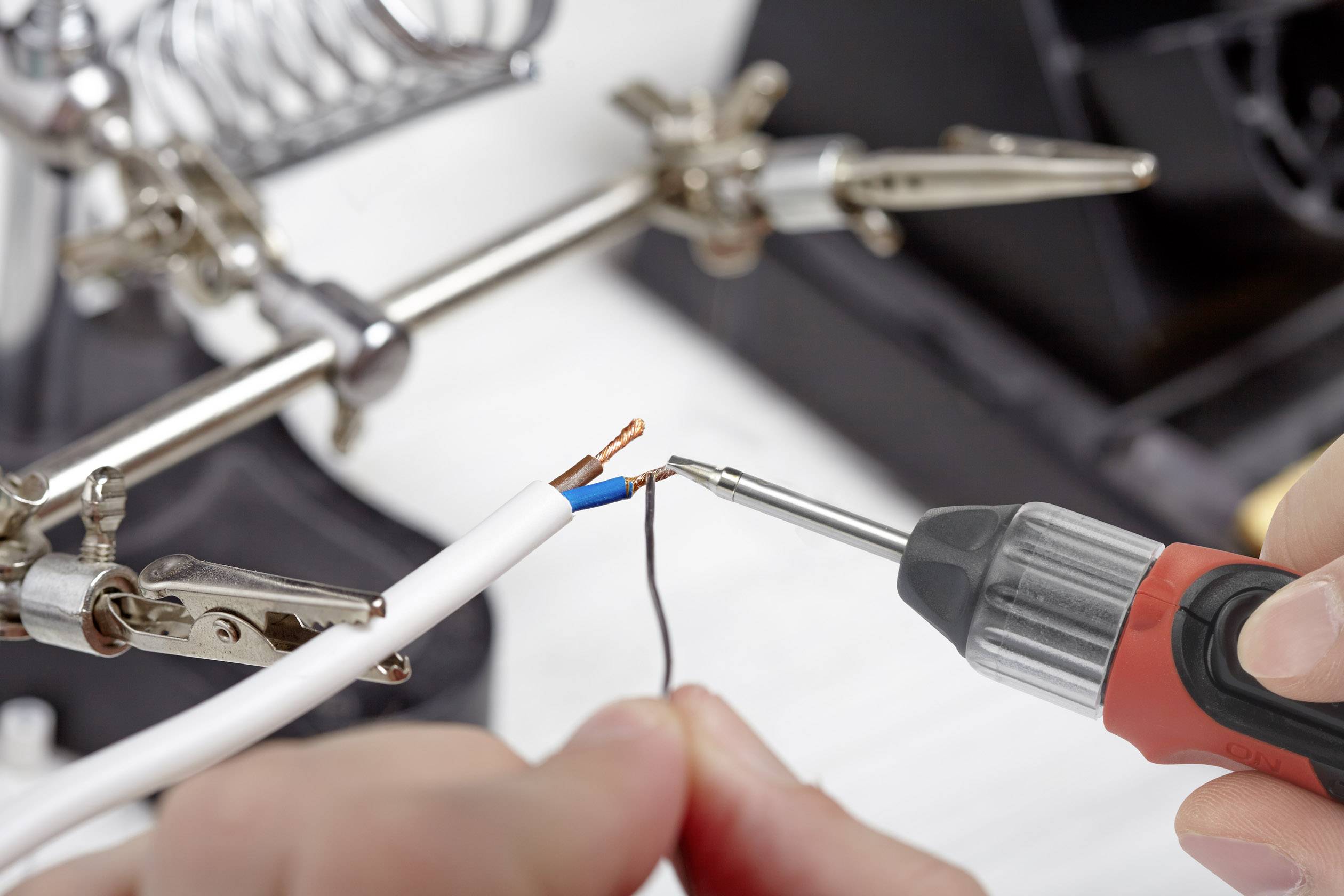 A person is holding a soldering iron to two exposed cable ends