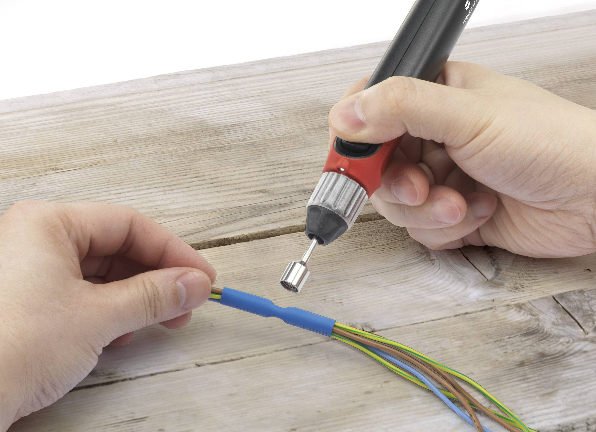 A person is holding a soldering iron and soldering wires on a wooden table.