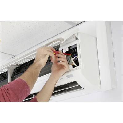 A person is repairing an air conditioning unit on the wall. Hands with a screwdriver are working inside the device.
