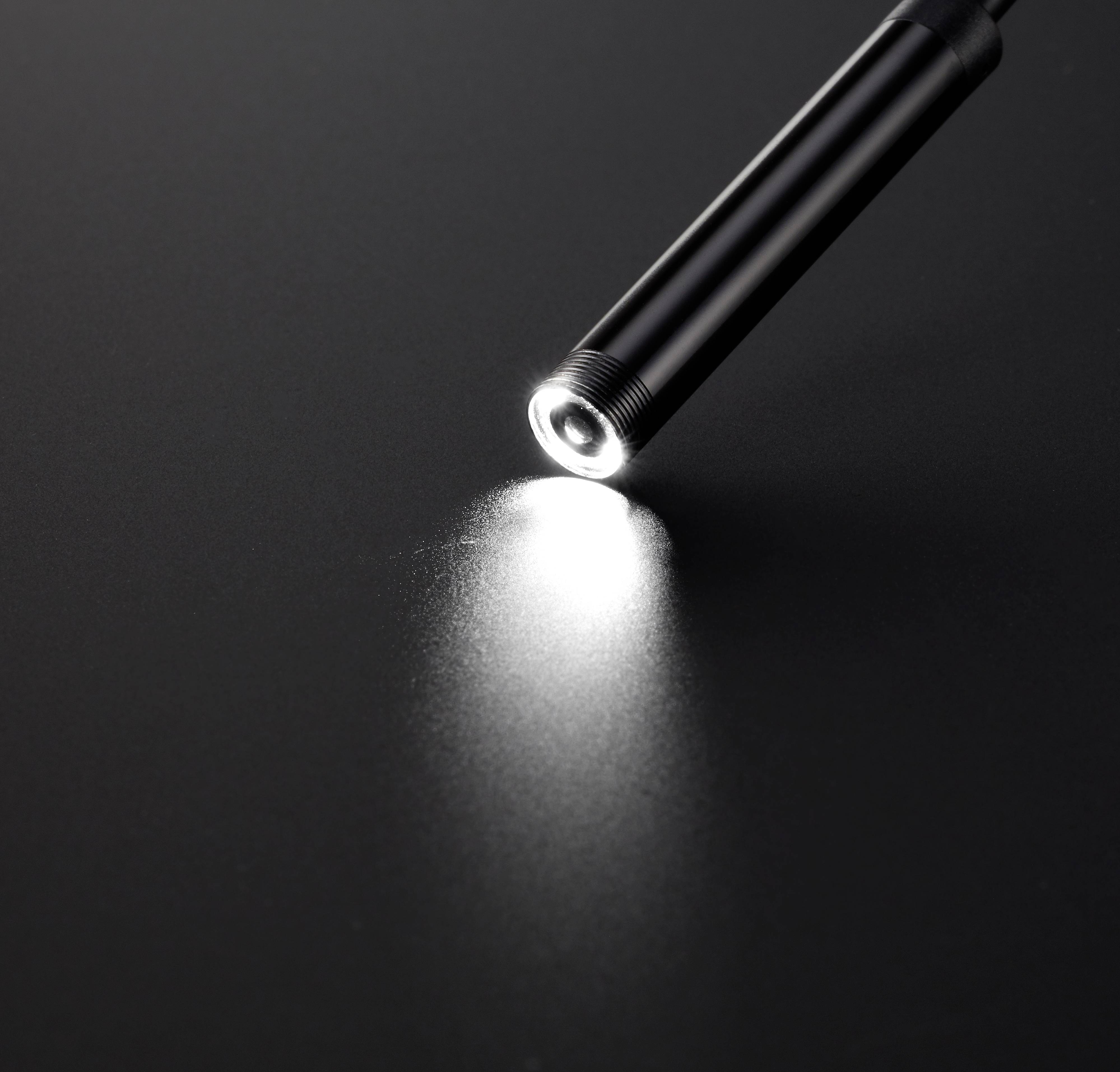 A pen with strong light shines on a dark surface and creates a small point of light.