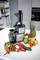 Juicer on a kitchen worktop, surrounded by fresh fruit and vegetables such as pineapple, grapes, lemons, carrots, and peppers.