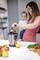 A woman is holding a baby while using a juicer to squeeze oranges. Fruits and vegetables are laid out on the table.