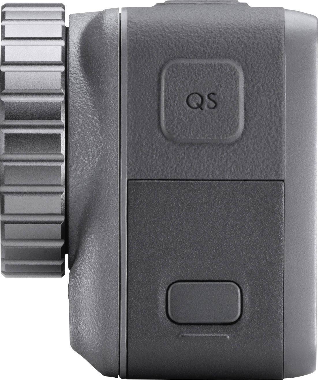 Side view of a grey camera with a round adjustment dial on the left side and 'QS' button on the top right.