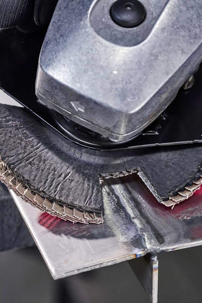 An angle grinder is working on a piece of metal. The grinding disc is removing material from the edge. Sparks can be seen.