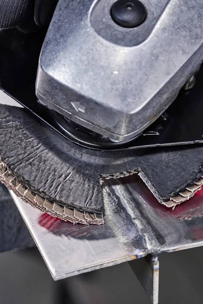 An electric grinding machine is machining a piece of metal. The grinding wheel shows visible signs of wear.