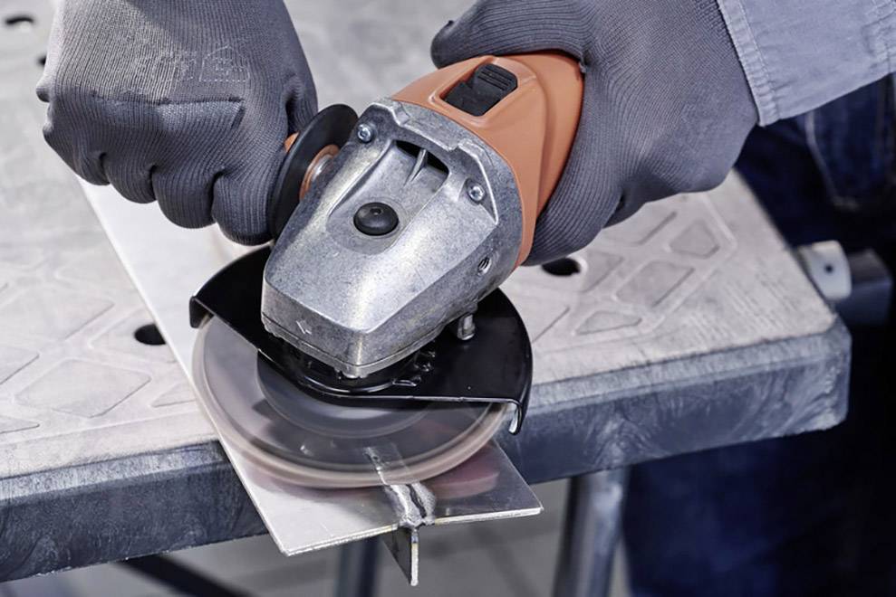 A person is working with an angle grinder to cut metal. Protective clothing is worn to ensure safety.
