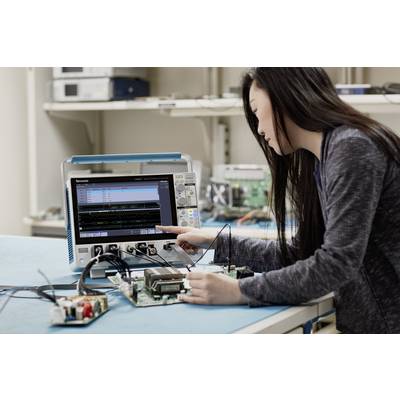 A person is working with an oscilloscope on a circuit board in a laboratory. They are checking electronic circuits.