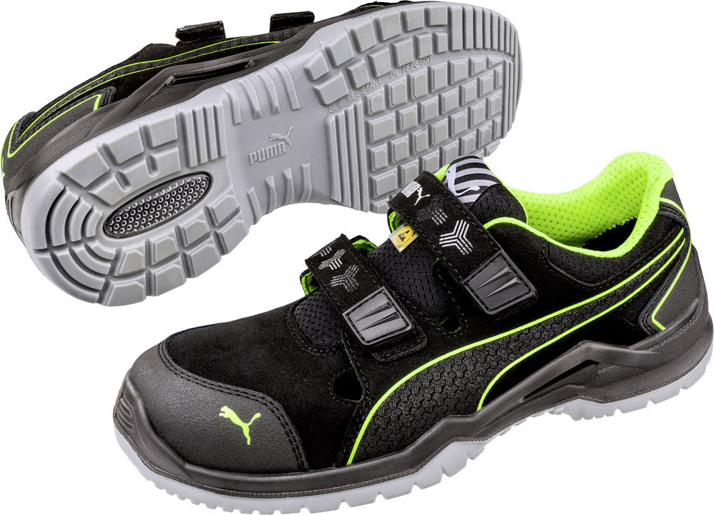 Black safety shoe with green accents and two hook and loop fasteners. Robust grey sole with non-slip tread. Suitable for work environments.