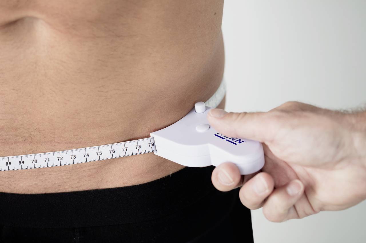 A tape measure is placed around a man's waist to measure his waist circumference.