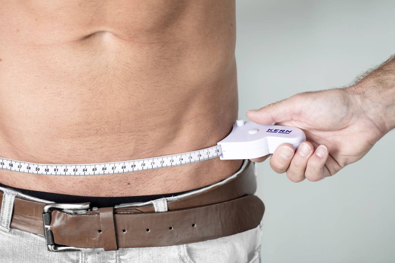 A man measures his waist circumference with a tape measure to check his health status.