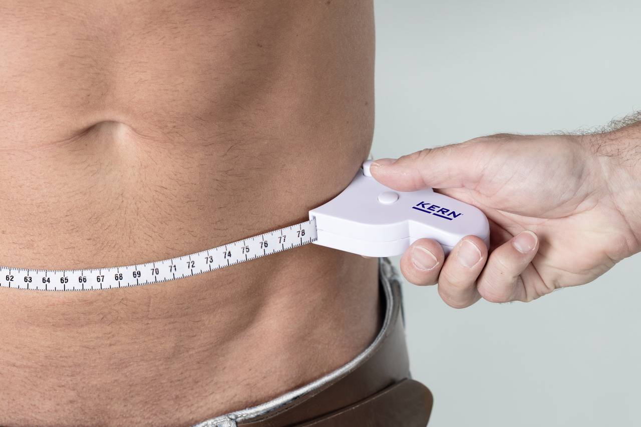 A man is being measured around the waist. One hand is holding a tape measure wrapped around his midriff.