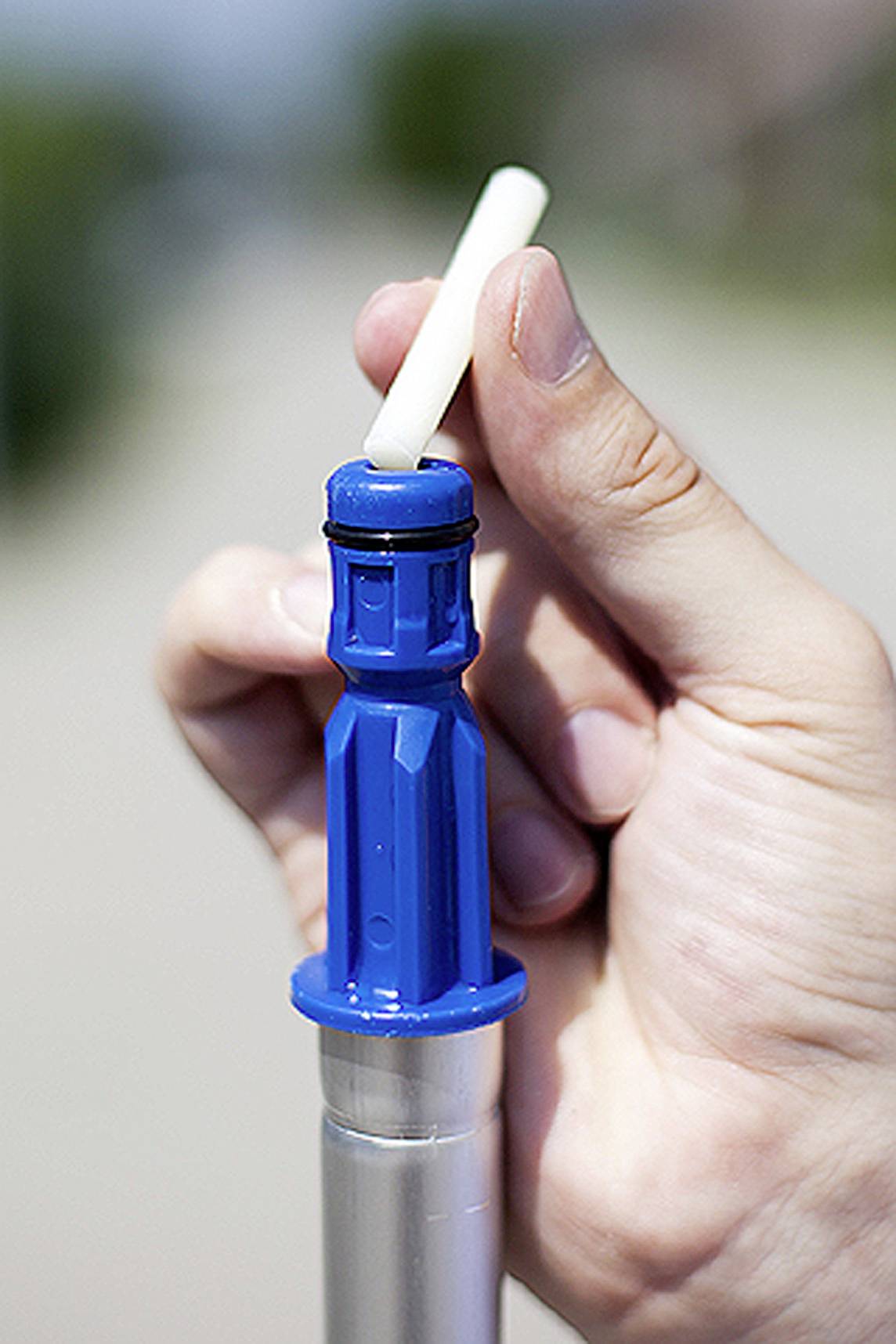A hand holds a blue water filter cartridge, ready to be inserted into a filter. Outside, with a blurred background.
