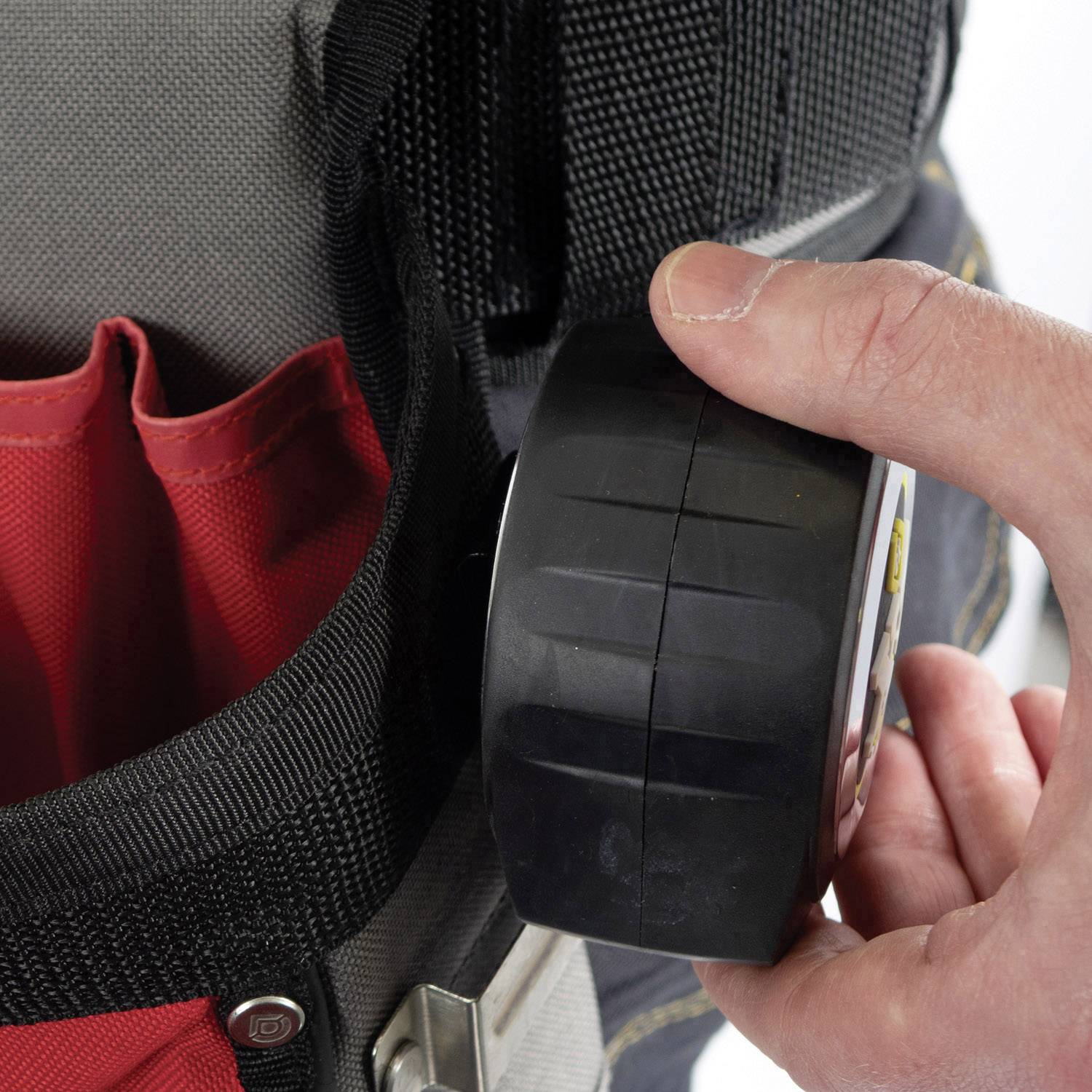 A hand is holding a black tape measure with a retractable tape protruding from a pocket in a toolbox.
