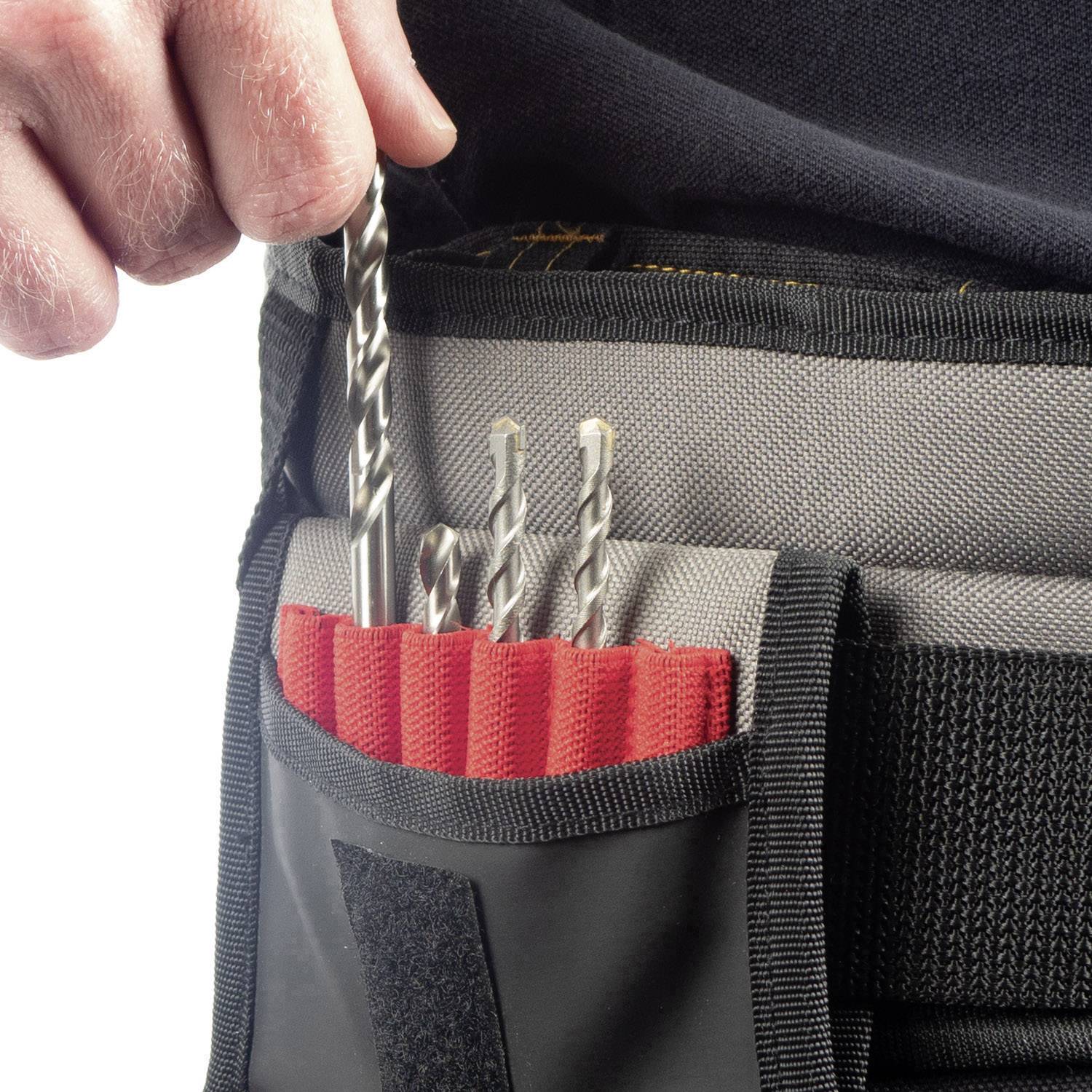 A hand is holding a drill in a protective sleeve with other drills in a red fabric cover.