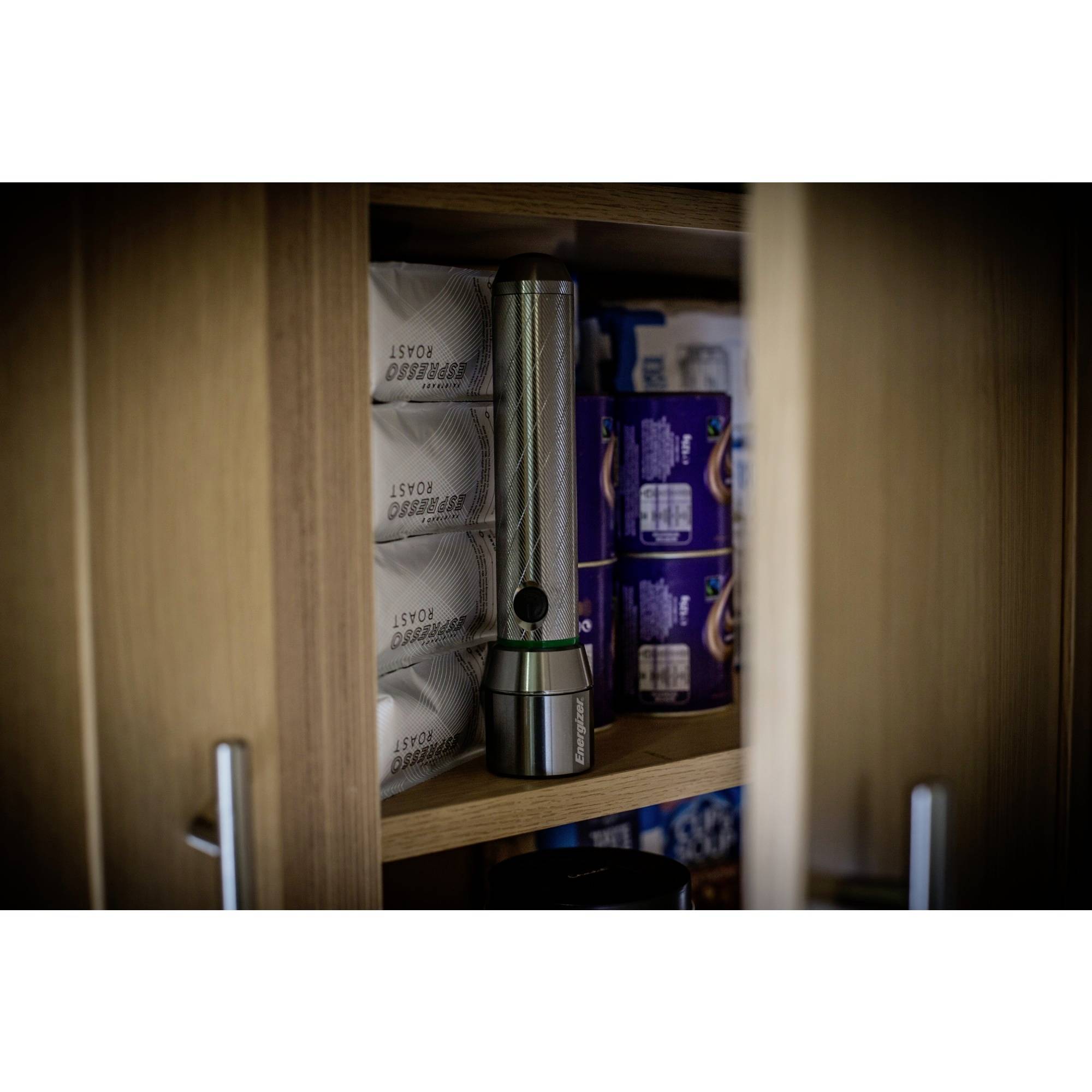 A torch stands upright in a cupboard between stacked toilet rolls, partially surrounded by wooden doors.