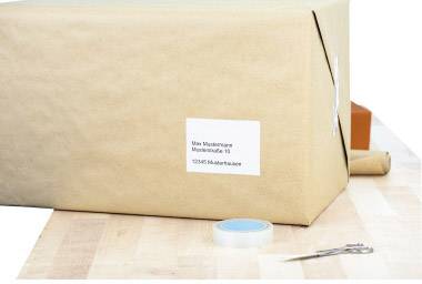 A large cardboard box wrapped in brown paper with a white address label is lying on a table; next to it are some sticky tape and scissors.