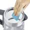 A hand is cleaning the inside of a kettle with a blue sponge. The kettle is made of metal and has a black handle.